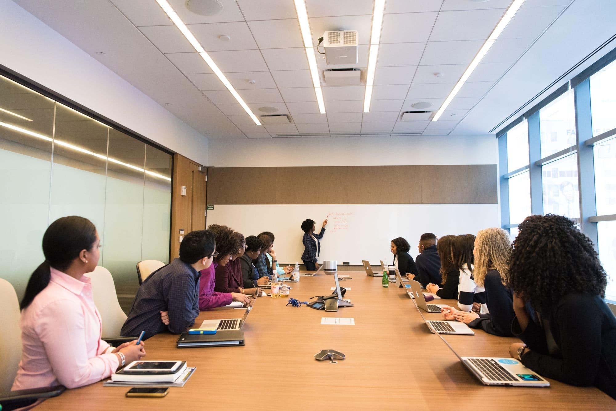 People working on laptops in a conference room whil looking at a woman presenting on a whiteboard